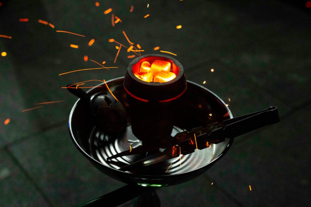 Close-up of glowing hookah coals with sparks in a dark setting, emphasizing warmth and relaxation.